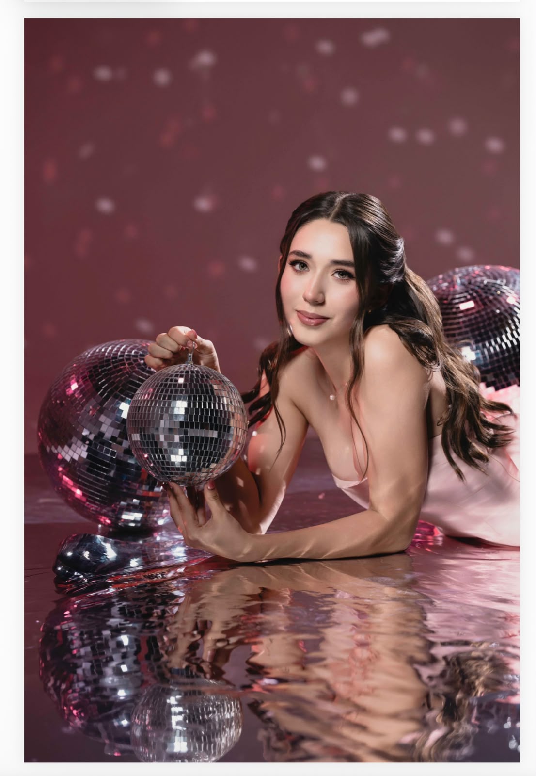 Natalia recostada junto a esferas disco, sobre fondo rosa