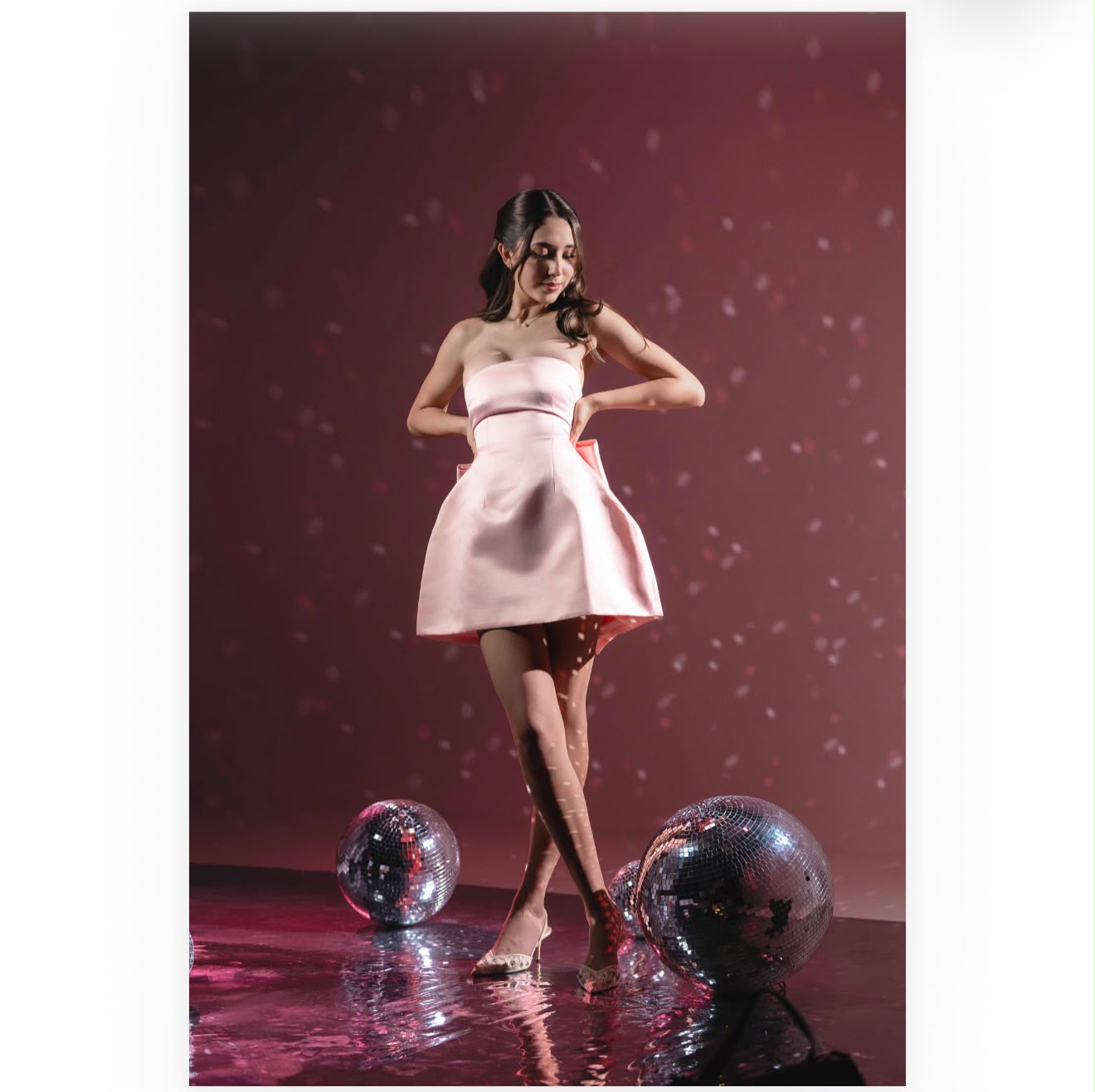 Natalia Aislinn de pie con vestido rosa junto a esferas disco